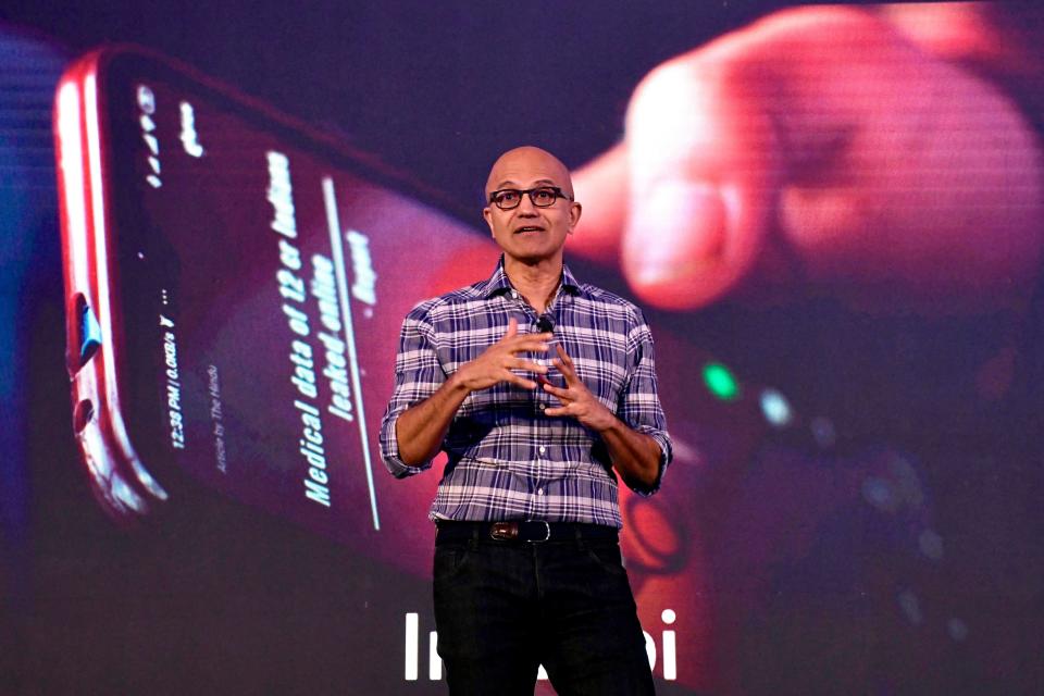 Satya Nadella speaks in front of the image of a cell phone.