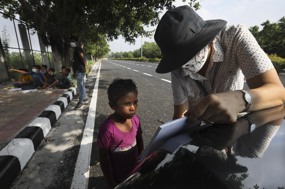 Veena Gupta teaches the English alphabets to a child on a sidewalk in New Delhi, India, on Sept. 3, 2020. It all began when Veena's maid complained that with schools shut, children in her impoverished community were running amok and wasting time. The street-side classes have grown as dozens of children showed keen interest. Now the Guptas, with help from their driver, teach three different groups three times a week, morning and evening. While many private schools switched to digital learning and online classes, children in most government-run schools either don’t have that option or don’t have the means to purchase digital learning tools like laptops and smartphones. (AP Photo/Manish Swarup)