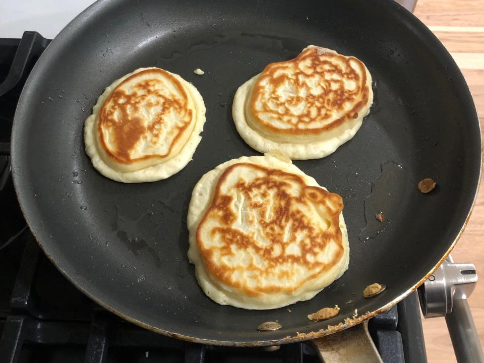 Three pancakes cooking in a black pan on a stove.