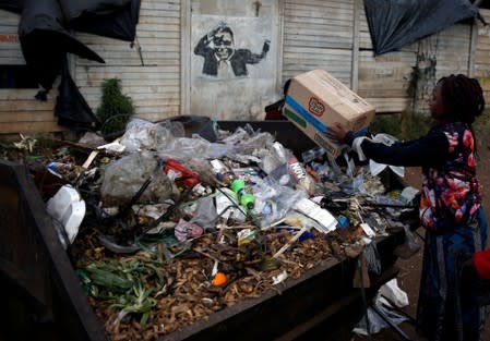 A woman dumps garbage in a bin besides a mural of late former Zimbabwe's President Robert Mugabe, in Mbare township, Harare