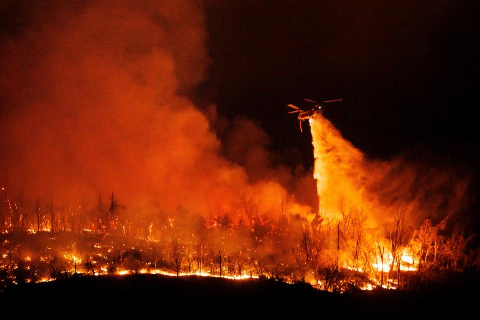 Helicopters try to douse the flames in a forested area of Butte County on Tuesday night (AP)