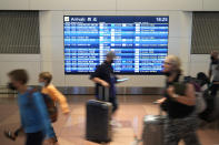 Flight passengers walk past a screen showing arrival schedules written in Chinese and English at the Haneda International Airport in Tokyo on Jan. 14, 2023. A hoped-for boom in Chinese tourism in Asia over next week’s Lunar New Year holidays looks set to be more of a blip as most travelers opt to stay inside China if they go anywhere. (AP Photo/Hiro Komae)