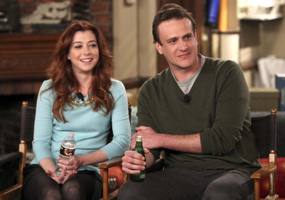 Alyson Hannigan and Jason Segel sitting, smiling in a casual setting with water and a beer