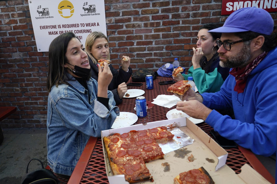 Bar owner Alejandra Benitez, left, chats with friends as she shares pizza with them while dining outdoors at L&B Spumoni Gardens, Sunday, Oct. 4, 2020, in the Brooklyn borough of New York. The restaurant is in a neighborhood that has seen a rise in coronavirus cases recently. New York's mayor said Sunday that he has asked the state for permission to close schools and reinstate restrictions on nonessential businesses in several neighborhoods, including this one, because of a resurgence of cases. If restrictions are imposed, the restaurant may be forced to shut down its outdoor dining and service takeout and delivery orders only. (AP Photo/Kathy Willens)