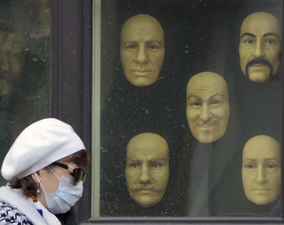 A woman wearing a face mask to protect against coronavirus walks past wax faces displayed in a window of a wax museum in St.Petersburg, Russia, Monday, May 4, 2020. (AP Photo/Dmitri Lovetsky)