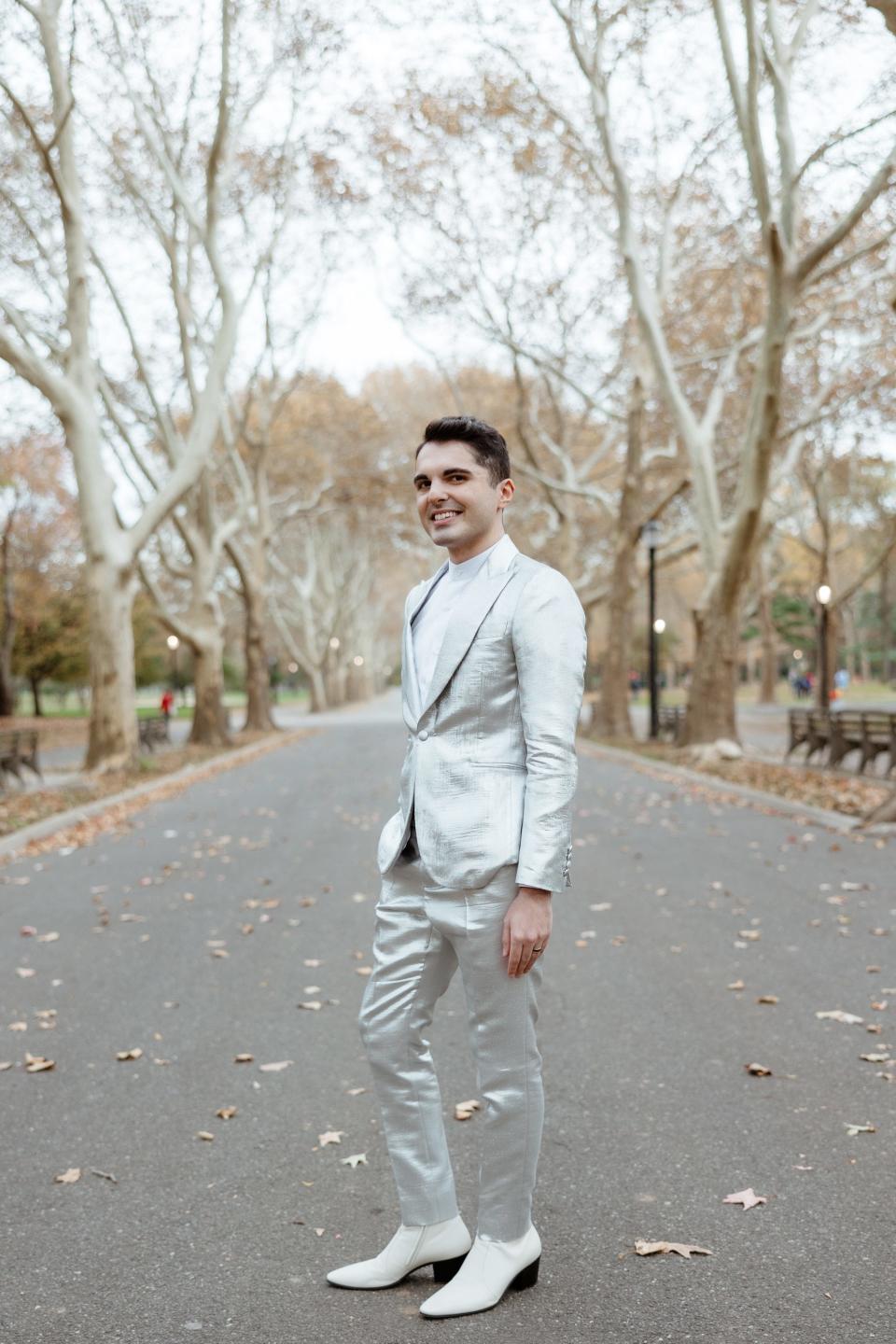 A man in a silver suit and white boots stands in a park.