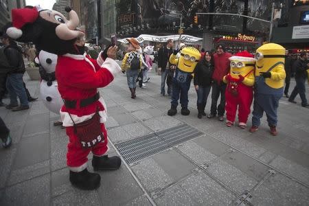 A man dressed up as Mickey Mouse takes a picture as people pose with others dressed up as Minion characters in Times Square in the Manhattan borough of New York, December 20, 2014. REUTERS/Carlo Allegri