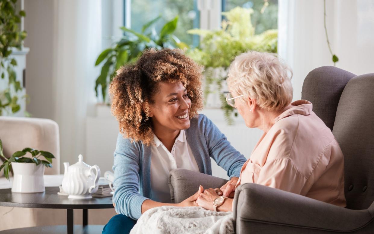 Female home caregiver talking with senior woman, sitting in living room and listening to her carefully