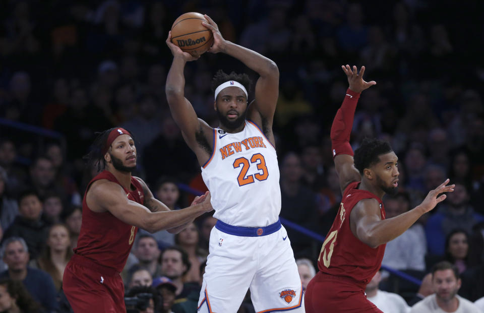 New York Knicks center Mitchell Robinson (23) grabs a rebound between Cleveland Cavaliers forward Lamar Stevens and guard Donovan Mitchell during the first half of an NBA basketball game, Sunday, Dec. 4, 2022, in New York. (AP Photo/John Munson)