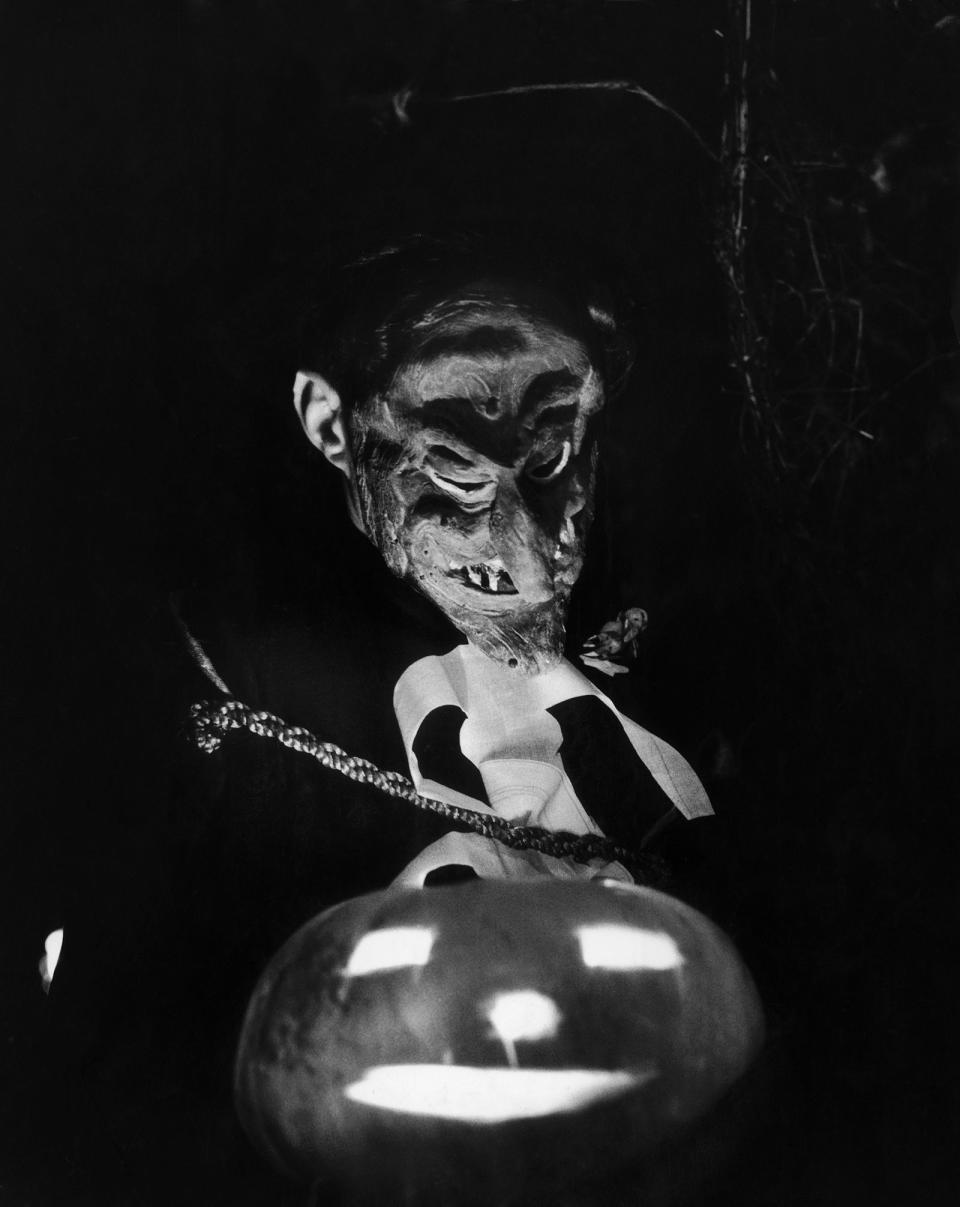 <p>A masked guest sits in front of a glowing pumpkin at a 1956 Halloween party.</p>