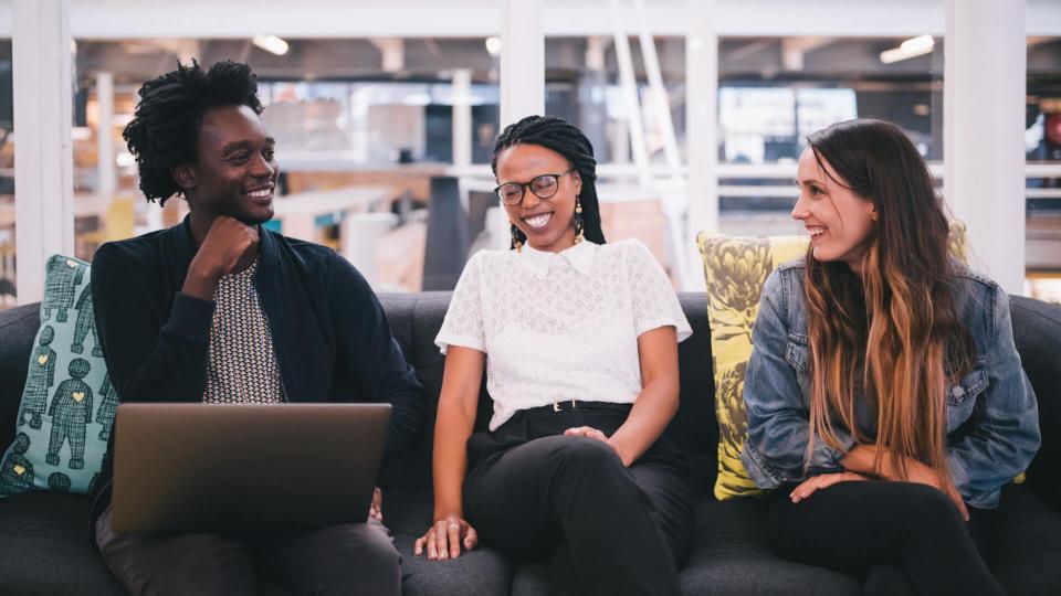 employees smiling while holding discussion on tech startup office couch