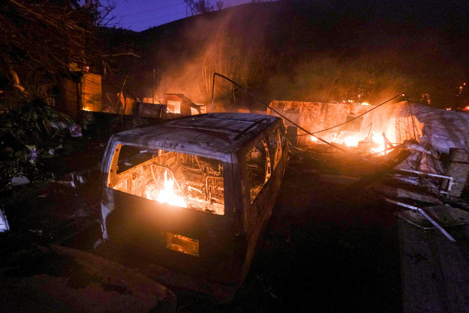 A small fire burns in the shell of a vehicle near a burning house at the South Fire in Lytle Creek near Rialto, Calif., in San Bernardino County on Wednesday, Aug. 25, 2021. (AP Photo/Ringo H.W. Chiu)