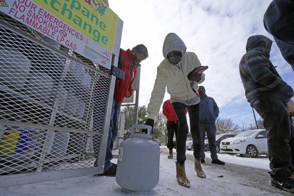 Christine Chapman, center, sets down an empty canister to exchange for a full propane tank from Robert Webster, left, outside a grocery store Tuesday, Feb. 16, 2021, in Dallas. Even though the store lost power, it was open for cash only sales. Chapman said she has been without power for two nights and is using the propane to keep warm. (AP Photo/LM Otero)