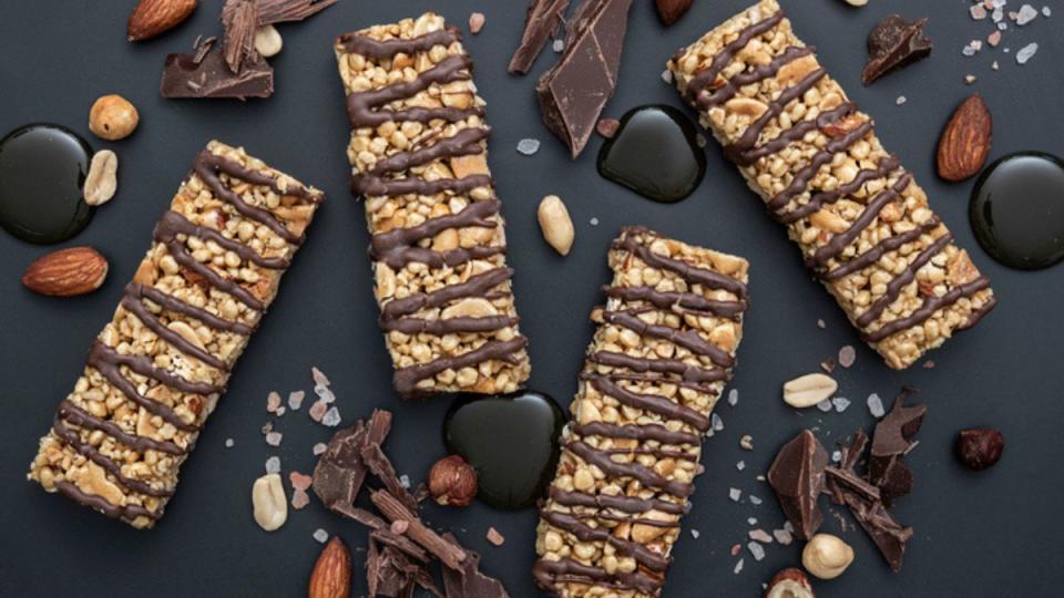 homemade granola bars with chocolate chips and drizzle against black background with nuts