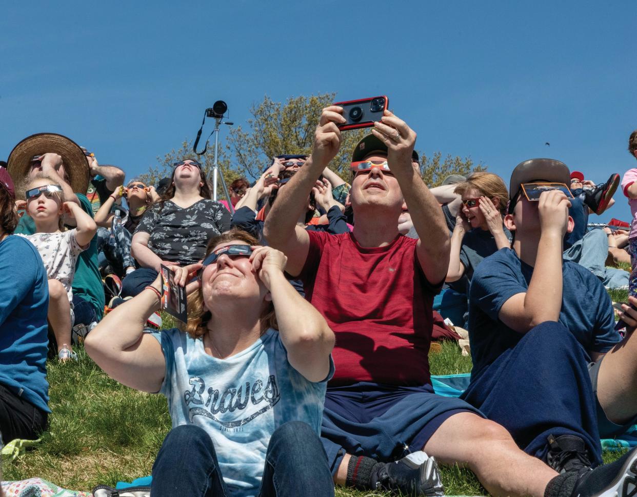 Spectators sit on a grass berm beyond the north end zone in Saluki Stadium watching the total eclipse in Carbondale, Illinois on April 8, 2024.