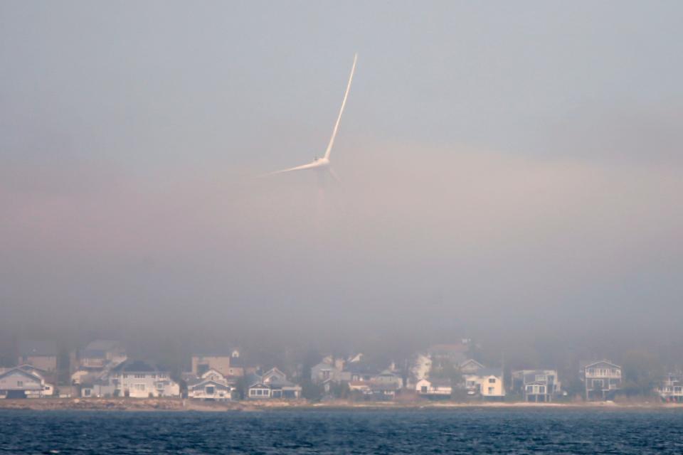 The wind turbine blade is seen hovering over a low cloud hanging over Fairhaven as seen from East Beach in New Bedford.