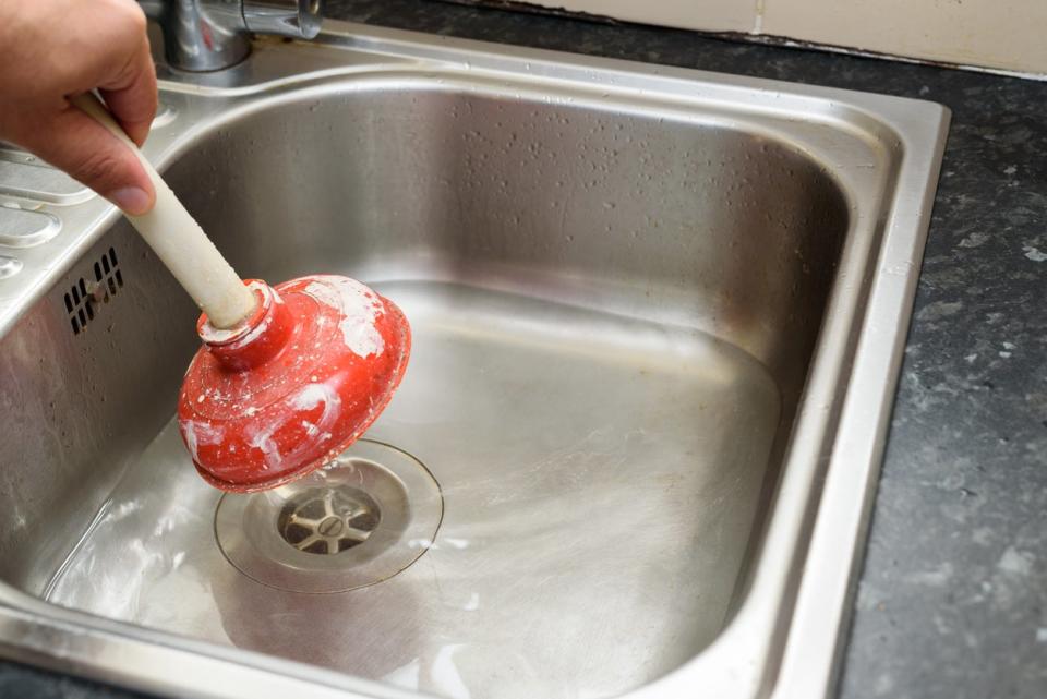Man using a plunger with one hand and water in kitchen sink.