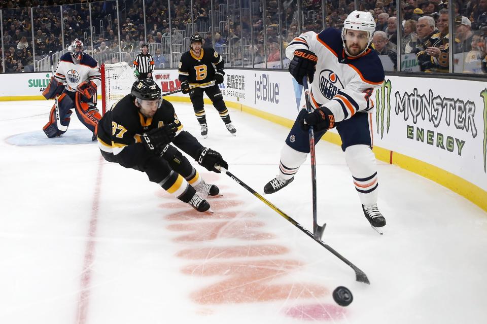 Edmonton Oilers' Kris Russell (4) plays the puck as Boston Bruins' Patrice Bergeron (37) skates in during the first period on an NHL hockey game in Boston, Saturday, Jan. 4, 2020. (AP Photo/Michael Dwyer)