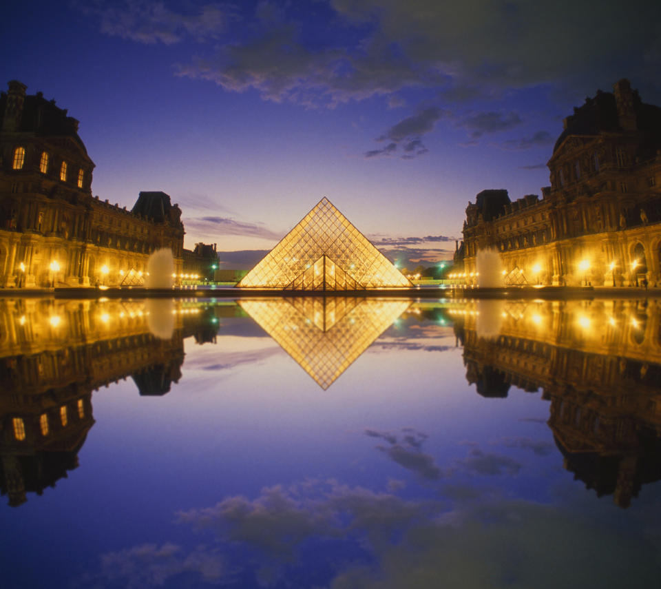 Louvre Glass Pyramid entrance and reflecting pond at sunset.