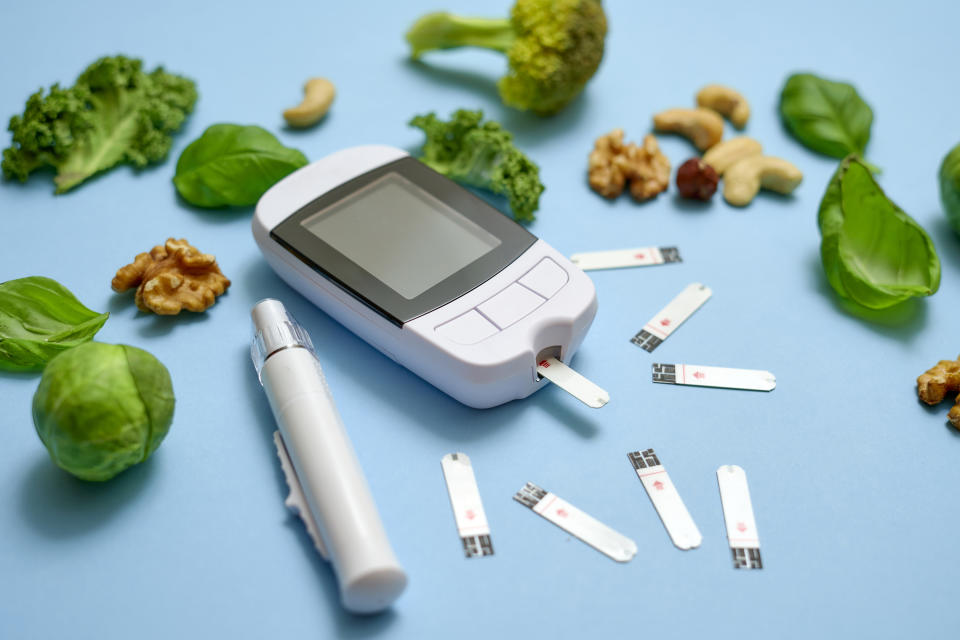 Young woman taking blood from her finger for blood sugar test. Close up shot on yellow background with vegetables on it.