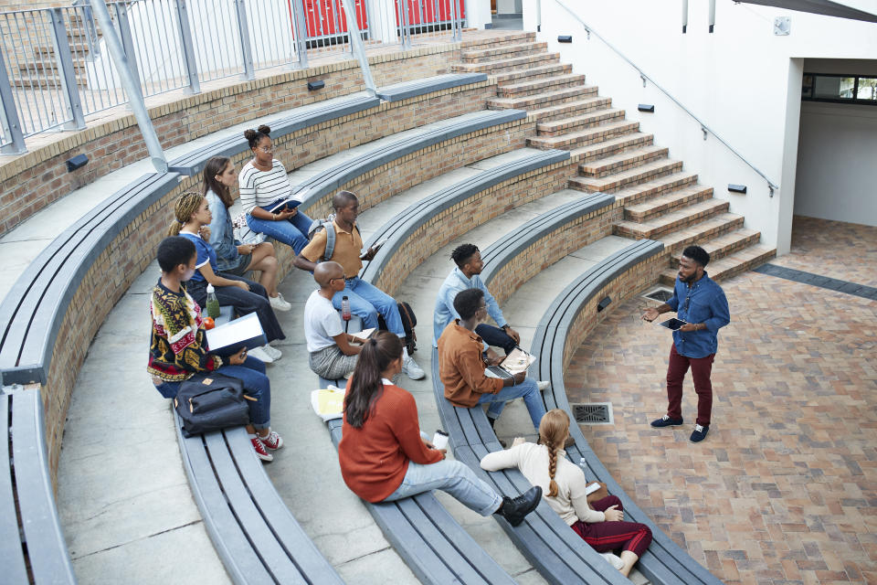 High angle view of male professor teaching young multi-ethnic students sitting on amphitheater steps at community college campus