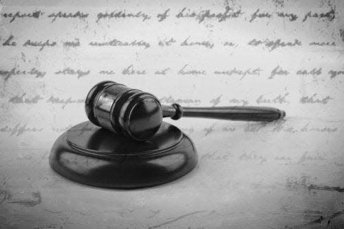 A judge's gavel sits atop a sound block, with the faded backdrop of cursive writing from historic documents.