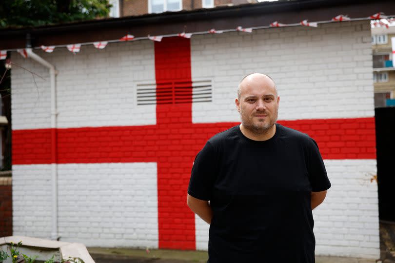 Chris Dowse poses for photos in the Kirby estate in front of a massive St. George's cross painted on a wall