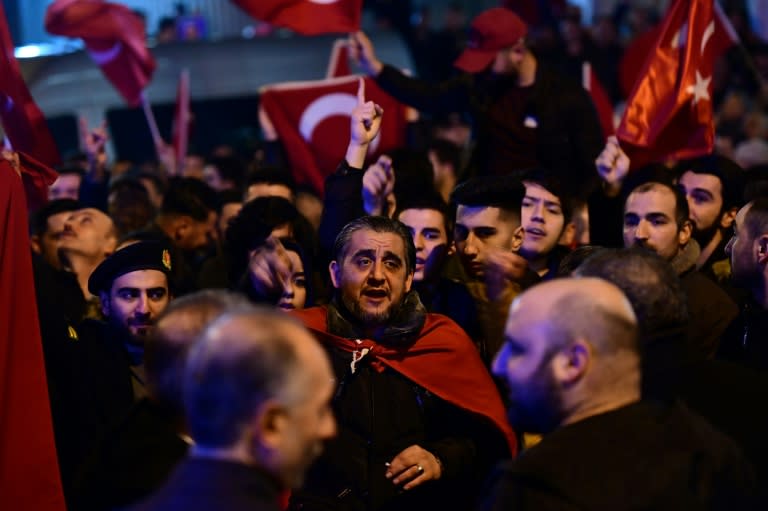 People gesture and wave flags as Turkish residents of the Netherlands gather for a protest outside Turkey's consulate in Rotterdam on March 11, 2017