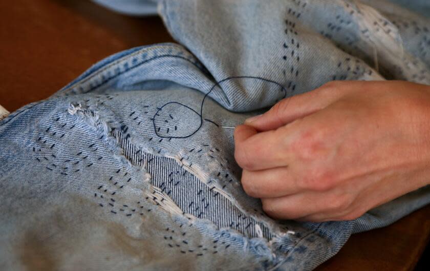 Kim Krempien, co-owner of Other Lives Studio, uses various sewing techniques to mend weathered jeans.