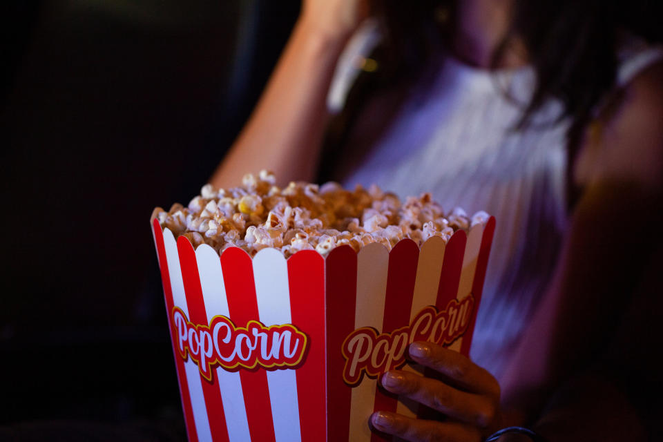 Person holding a large striped popcorn box at a movie theater, evoking a dating atmosphere