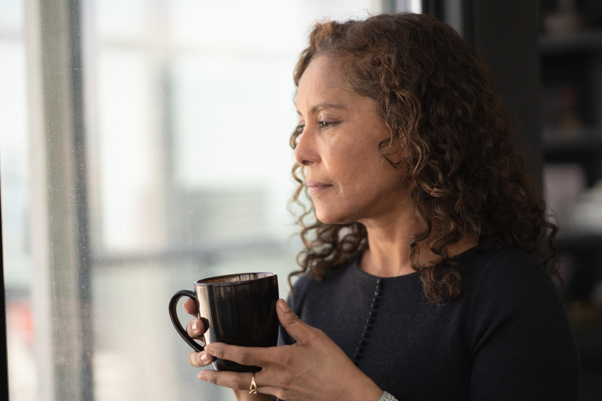 A middle-aged woman holds a coffee mug as she looks off into the distance.