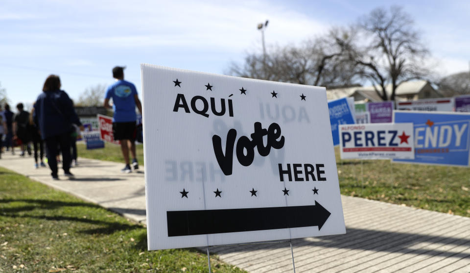 In this Friday, Feb. 28, 2020 photo, pedestrians pass signs near a polling site in San Antonio. California and Texas are the most populous states in the nation and the biggest delegate prizes for the candidates, yet they also present a stark contrast in voting laws. (AP Photo/Eric Gay)