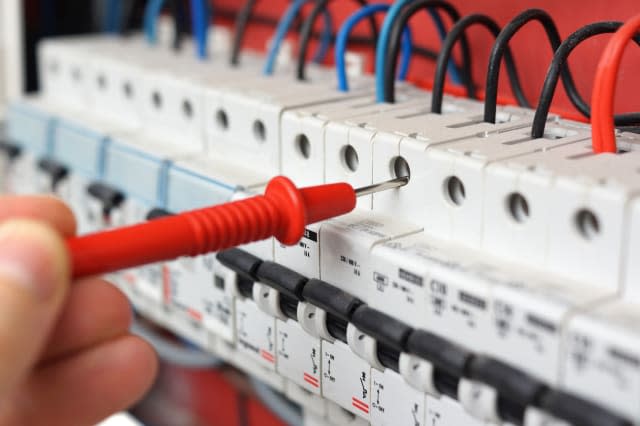 Hand of an electrician with multimeter probe at an electrical switchgear cabinet