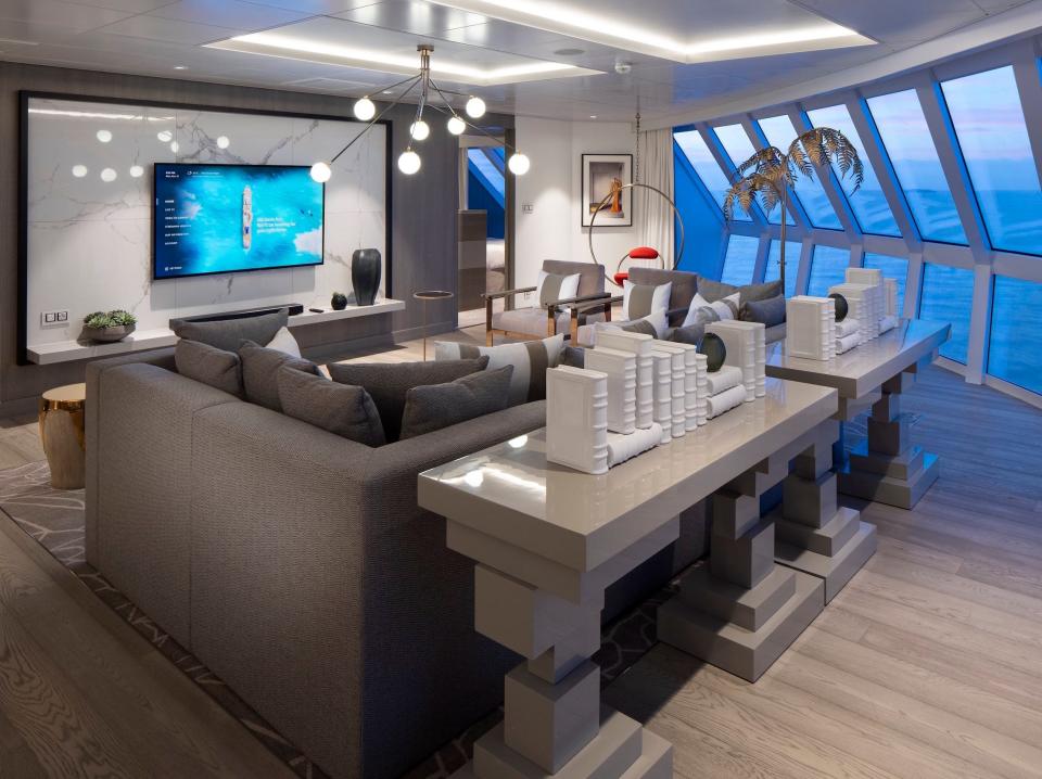 a couch facing a TV and tables behind the couch next to panoramic windows in the Iconic suite aboard the Celebrity Apex cruise ship