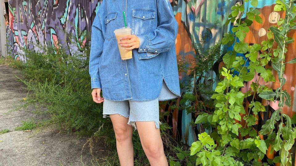 Gigi Hadid wears denim shorts and a denim shirt while holding an ice coffee