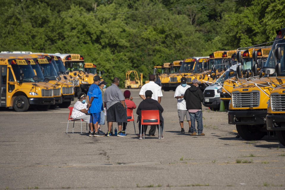 Workers sit amid dozens of idle school buses after demonstrators blocked the driveways of the Detroit Public Schools West Side Bus Terminal on the first day of summer school on Monday.  (David Guralnick / The Detroit News via AP)