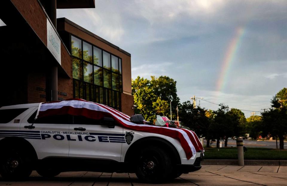 A rainbow is seen behind the police vehicle that draped in an American flag outside the police station on North Tryon on Tuesday, April 30, 2024. Flowers have been placed on the hood in memory of CMPD officer Joshua Eyer, who was killed in yesterday’s deadly shootout in East Charlotte.