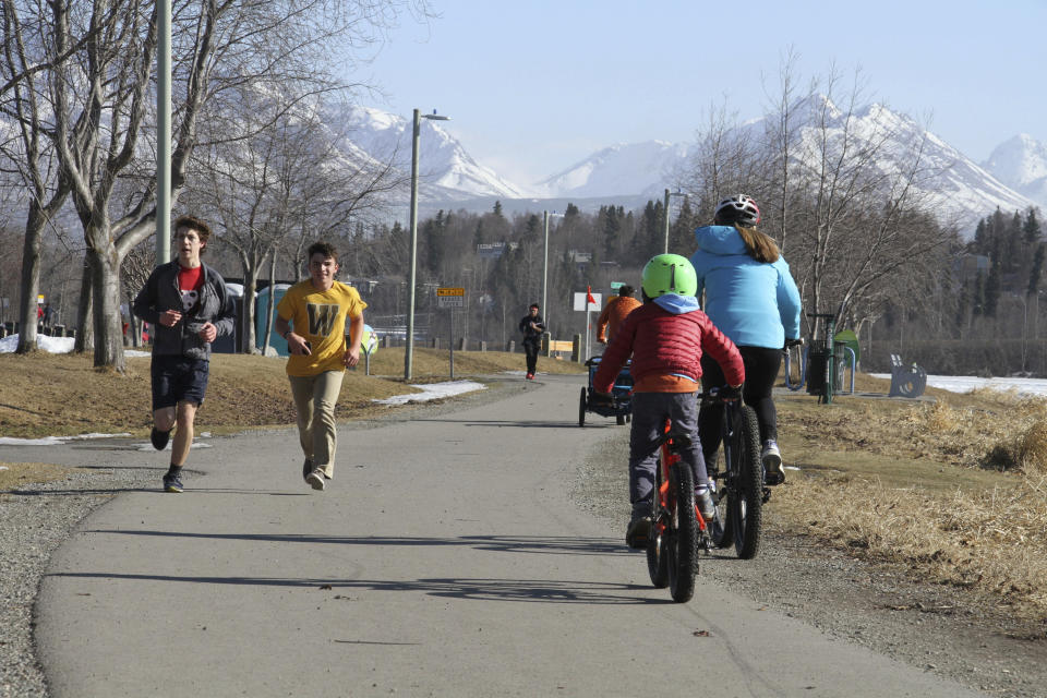 This April 3, 2019, photo shows people running and biking at Westchester Lagoon in Anchorage, Alaska, with the snow-covered Chugach Mountains in the distance. Much of Anchorage's snow disappeared as Alaska experienced unseasonably warm weather in March. (AP Photo/Mark Thiessen)