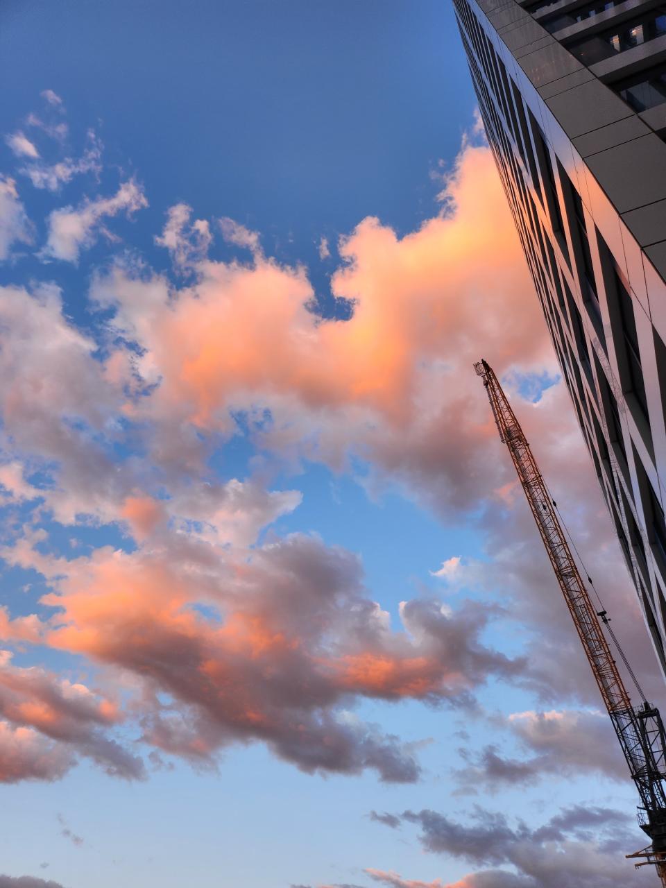 <p>A picture taken with the Galaxy Z Flip 4 showing a tall building against pink fluffy clouds and a crane next to it.</p>
