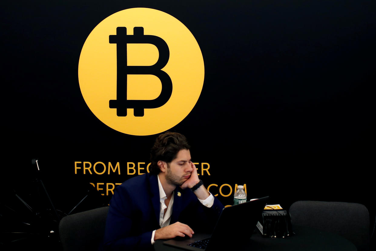 A man works on a laptop beneath the Bitcoin logo at the Consensus 2018 blockchain technology conference in New York City, New York, U.S., May 16, 2018. REUTERS/Mike Segar