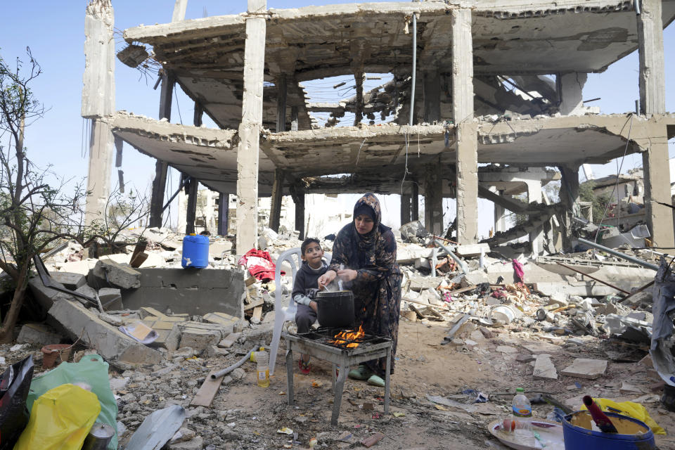 Palestinian woman Hiyam Qudih cooks in front of her family's building destroyed in the Israeli bombardment of the Gaza Strip in the village of Khuza'a, east of Khan Younis, Gaza Strip, Sunday, Nov. 26, 2023. on the third day of the temporary ceasefire between Hamas and Israel. (AP Photo/Adel Hana)