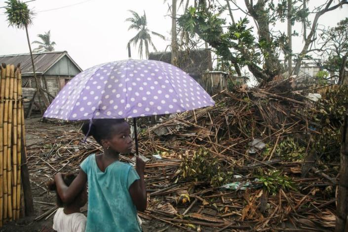 Two small children look at the remains of a building, one holds an umbrella.