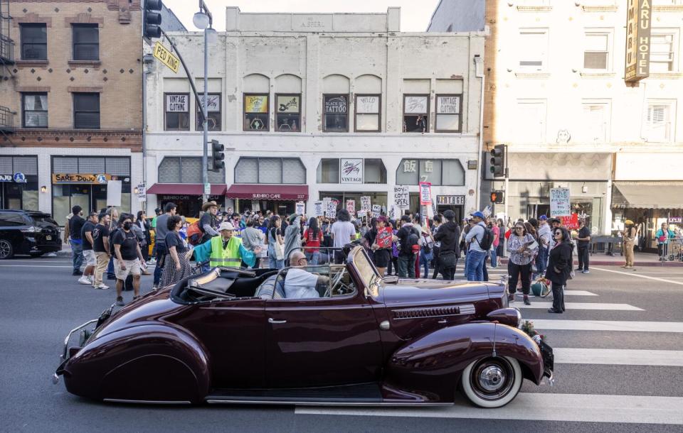 People holding signs and a classic car in a crosswalk.