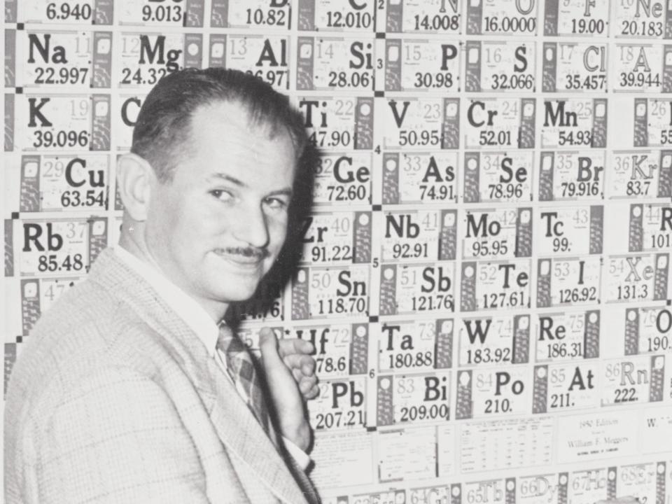 Nobel Prize winner Edwin McMillan at the University of California laboratory in front of a large periodic table of elements