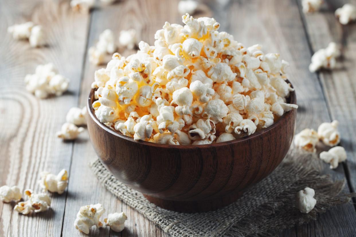 A wooden bowl of salted popcorn at the old wooden table. Dark background. selective focus.