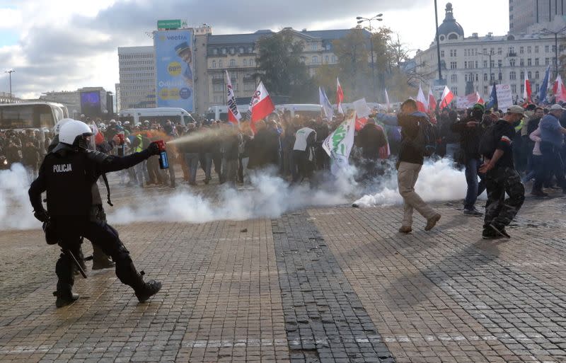 A policeman sprays demonstrators with tear gas during anti lockdown protest in Warsaw