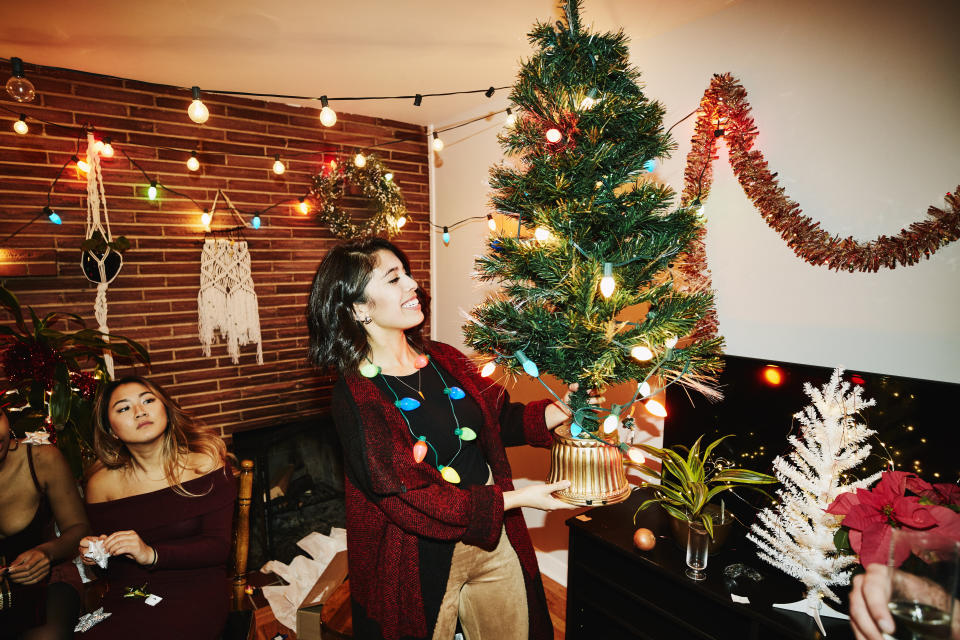 Smiling woman holding miniature Christmas tree during holiday party with friends