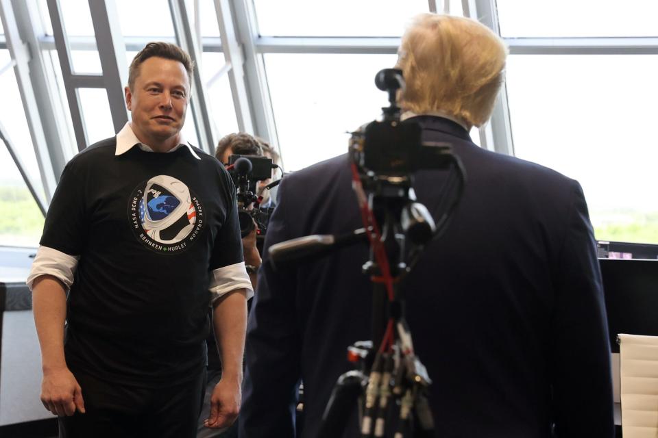 Elon Musk stands facing Donald Trump, whose