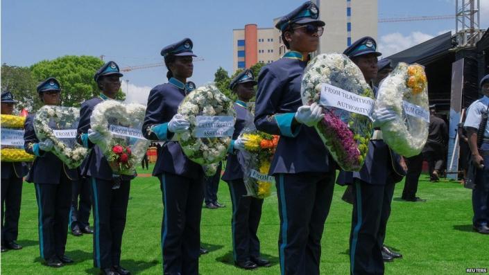 State employees in uniform hold wreaths of flowers