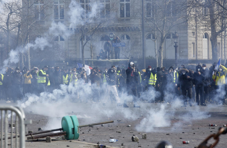Youths walk through tear gas during a yellow vests demonstration Saturday, March 16, 2019 in Paris. French yellow vest protesters clashed Saturday with riot police near the Arc de Triomphe as they kicked off their 18th straight weekend of demonstrations against President Emmanuel Macron. (AP Photo/Christophe Ena)